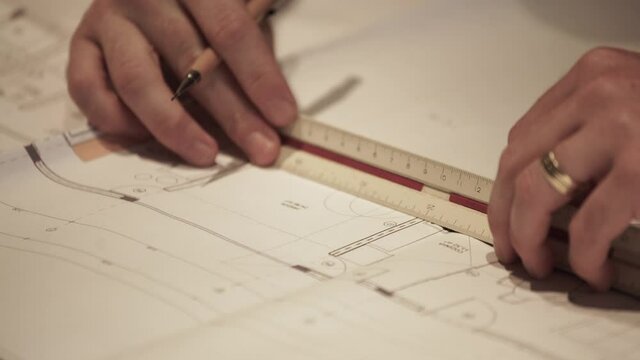 Close up of architect measuring details on architectural blueprint, using scale ruler and taking notes of the project 