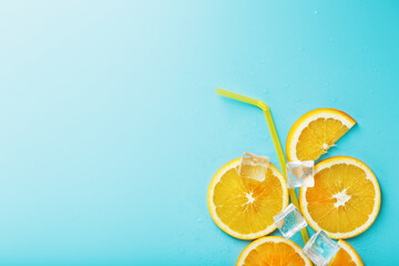 A composition of orange slices and ice cubes with a straw on a blue background in the form of a refreshing drink