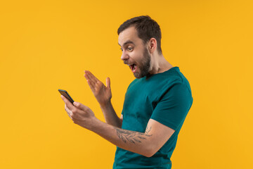 Studio portrait of happy young bearded man reading message notificationon his smartphone with excited face expression glad to know he hit the jackpot in online lottery