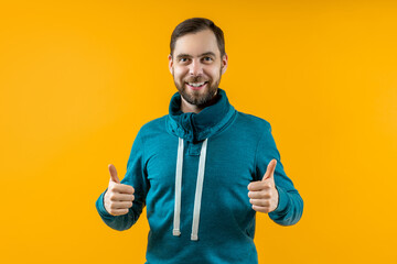 Studio image of young bearded man showing thumbs up, isolated over yellow background