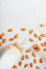 Almond milk in a glass bottle on a light background with a scattering of seed kernels and a wooden spoon.