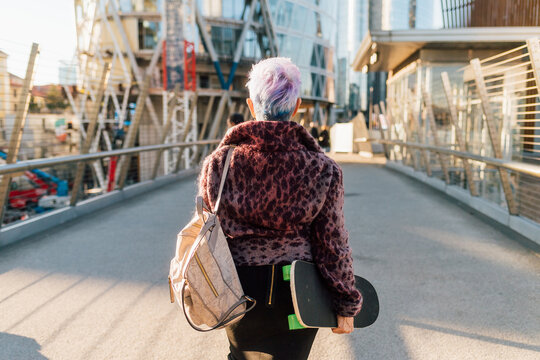 Italy, Rear view of fashionable senior woman with skateboardin city