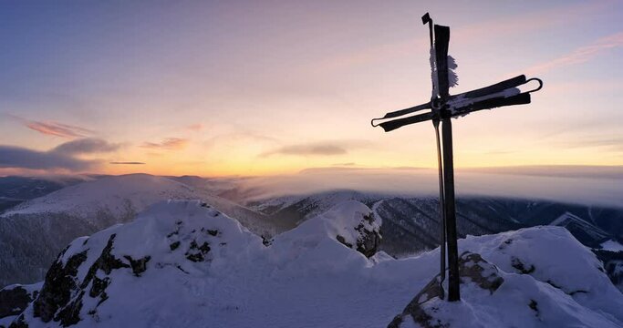 Christian cross in a snowy mountain landscape. Clouds spill over the hills at dusk.