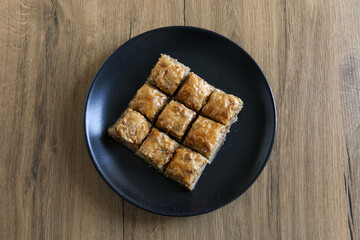 Baklava, traditional Turkish dessert named as Baklava in a black plate on a wooden background. Selective focus on the center baklava. Ramadan concept and idea.