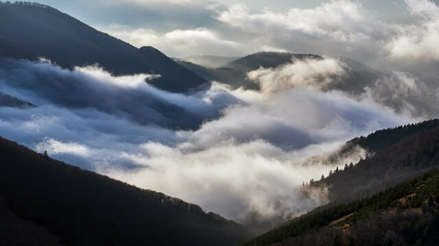 Clouds spill over the tops of the hills in the light of the rising sun, Mystical Atmosphere