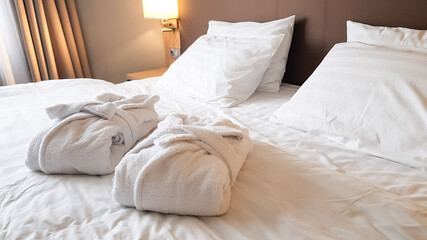 2 snow-white bath robes, beautifully folded, lie on a bed covered with white linen.