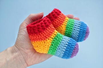 Rainbow handmade crochet socks on a hands. Baby shower party decor. First birthday, newborn gift