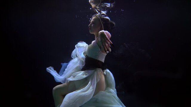sexy young lady is swimming alone in dark deepness, whirling slowly underwater