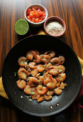 Shrimp portion. Brazilian food. Frying pan with shrimp with sides tomato, farofa and lemon.
