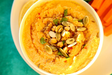 Hummus in a white plate with carrots, lemon and spices