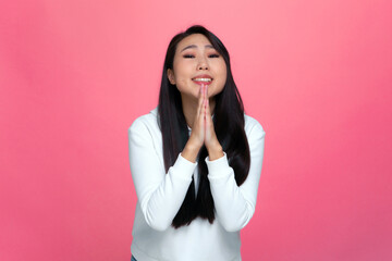 Pretty young asian girl pleading begging keeping palms together, pray for favor, ask for help on pink studio background