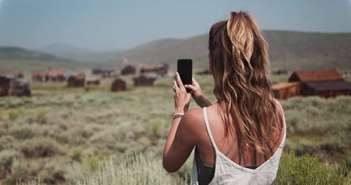 Female tourist taking a picture with her phone of a gold mining town in the California desert on vacation