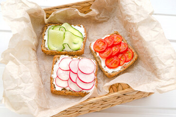 delicious vegetarian sandwiches with cream cheese, fresh cucumber, radish, tomatoes in a wicker basket on a white wooden background. Flat lay. healthy food diet slimming fitness. close-up