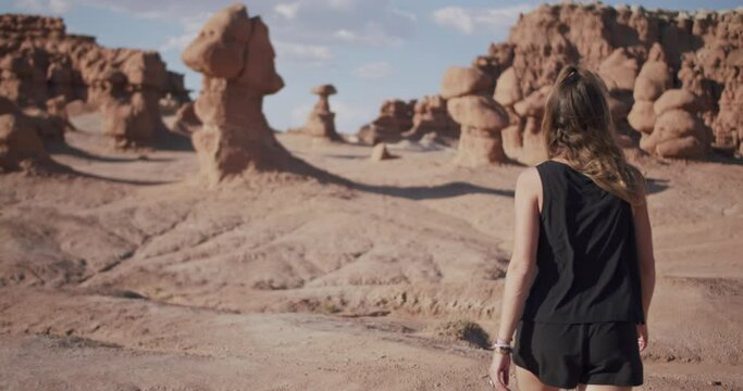 Young female hiker exploring Goblin Valley State Park in the desert while walking through hoodoo rock formations, slow motion
