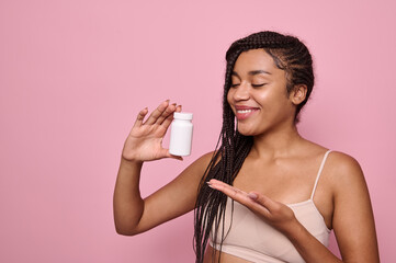 Attractive woman smiles pointing on a white container with dietary supplements or vitamins for...