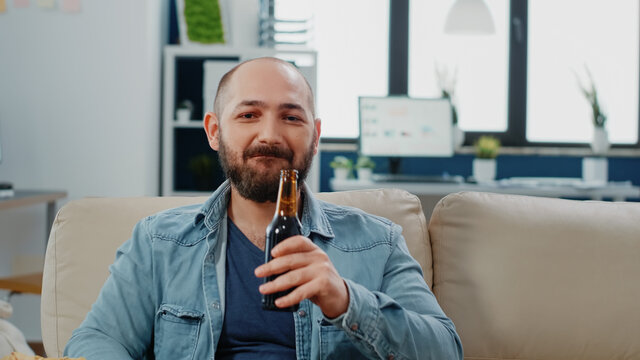 Portrait Of Man Drinking Beer From Bottle And Enjoying Free Time After Work At Office. Cheerful Person Looking At Camera And Having Alcoholic Beverage To Do Fun Activity After Hours.