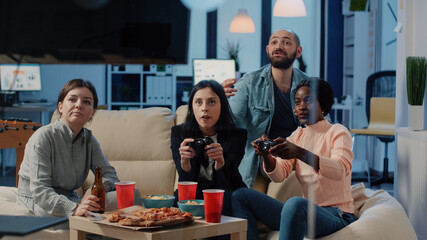 Frustrated colleagues playing video games and losing, enjoying free time after work. Coworkers using controllers on tv console to do fun activity while celebrating with drinks and snacks