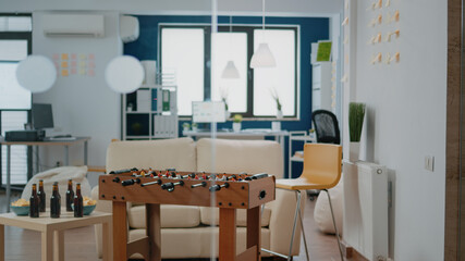 Nobody in workplace with fun activity for meeting after work. Empty office with foosball game table to play football after hours and drink bottles of beer. Celebration with colleagues