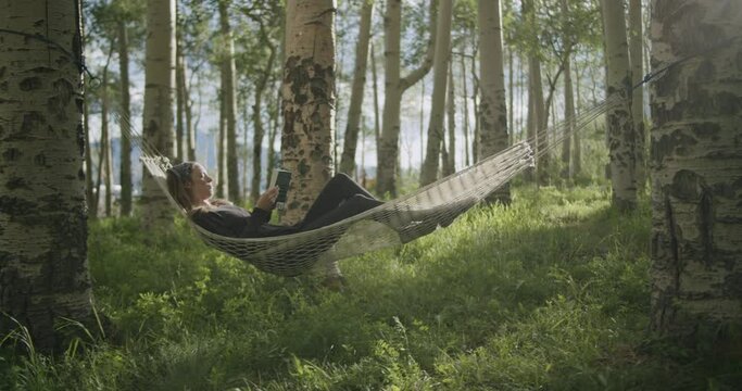 Young woman relaxing in hammock and reading a book at sunset in a beautiful birch forest in the wilderness outside of Telluride Colorado off of Last Dollar Road