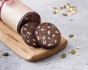 Chocolate sausage with oatmeal and seeds on gray textured background. Delicious healthy vegan dessert