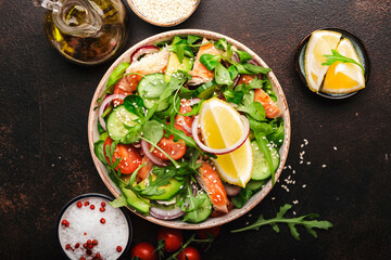 Fototapeta na wymiar Fresh Salad with chicken, tomatoes, arugula, onion, avocado, sesame seeds and lemon oil dressing. Healthy food. Top view. Brown table