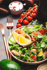 Fresh Salad with chicken, tomatoes, arugula, onion, avocado, sesame seeds and lemon oil dressing. Healthy food. Top view. Brown table