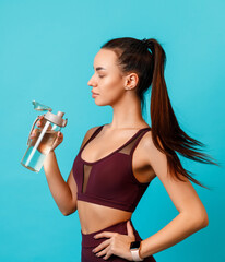 beautiful young brunette woman in sportswear stands with a bottle of water on a blue background