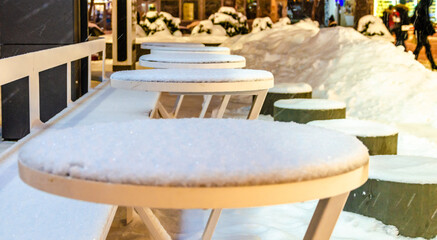 Outdoor cafe tables under the snow in the winter evening.