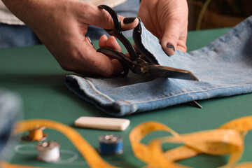 Seamstress cutting jeans with scissors for hemming