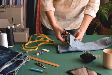 Seamstress cutting jeans with scissors for hemming