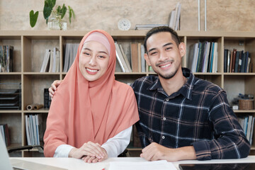 Portrait of entrepreneur business startup persons, young male, and beautiful female owner, two partners who Islamic couple, looking at camera, smiles happily in small e-commerce workplace office.