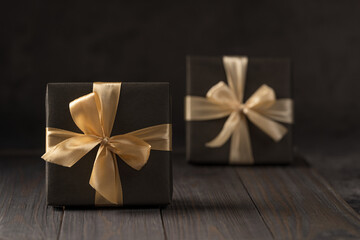 two boxes with gifts, wrapped in brown paper and tied with a gold ribbon, on a dark background,...
