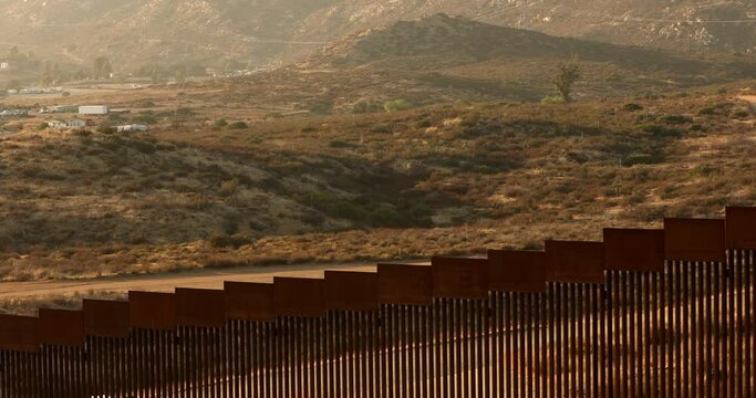 Tecate, Baja California, Mexico - September 14, 2021: Late afternoon sun shines on the USA Mexico border wall as it winds through Tecate.