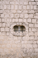 Fototapeta na wymiar Small oval window with a lattice on the old stone facade of the building