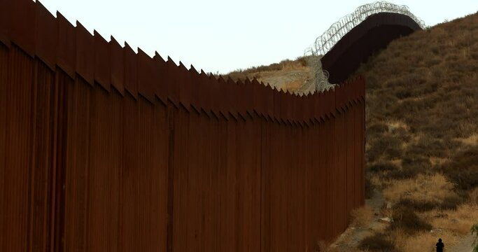 Tecate, Baja California, Mexico - September 14, 2021: Late afternoon sun shines on the USA Mexico border wall as it winds through Tecate.