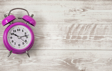 Purple alarm clock on a white wooden background. Flat lay