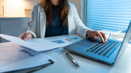 Overwork Concept The woman doing her work at late night by reading papers and typing them on the notebook