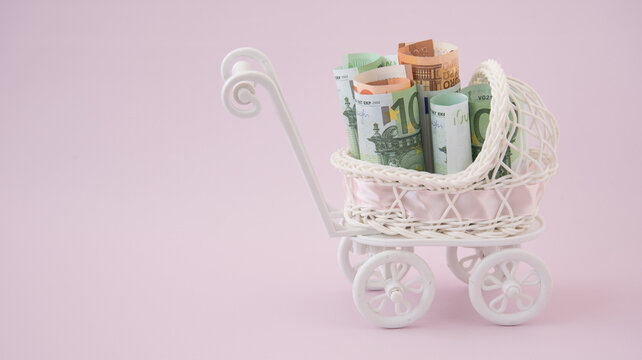 In the baby stroller there are euro bills. The concept of spending on a newborn. The concept of assistance during pregnancy and childbirth. Benefits and payments. Surrogacy. There's room for text.