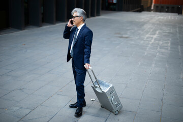 Senior businessman outdoors. Middle-aged businessman talking to the phone. Handsome man in suit using the phone