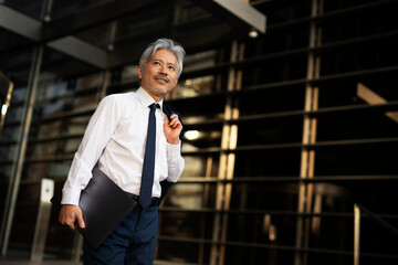 Portrait of senior businessman with laptop. Handsome man in suit outdoors....