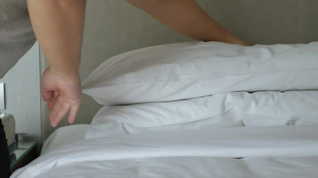 hotel service concept, housekeeper man arrange the pillow on the bed with white sheet, make bed in morning