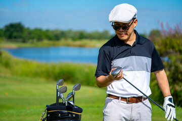 Portrait of Smiling Asian man holding golf club standing on golf course fairway in sunny day....