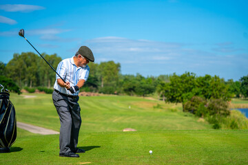 Asian senior man holding golf club hitting golf ball on fairway at country club in sunny day....