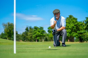 Asian senior man holding golf club hitting golf ball on fairway at country club in sunny day....