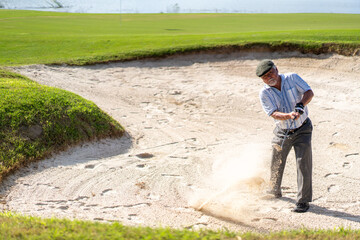 Asian people senior man hitting golf ball from a bunker on golf course to the green. Healthy elderly male golfer enjoy leisure activity outdoor sport golfing at golf country club in summer vacation