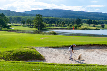 Confidence Asian man hitting golf ball from a bunker to the green at golf course in sunny day. Healthy male golfer enjoy leisure activity outdoor sport golfing at golf country club in summer vacation