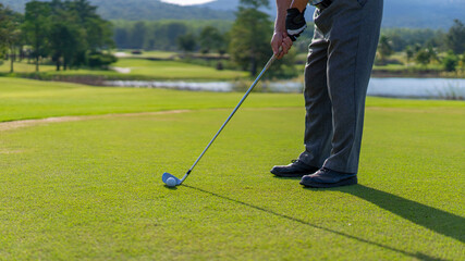 Fototapeta premium Asian senior man holding golf club hitting golf ball on fairway at country club in sunny day. Healthy elderly male golfer enjoy outdoor activity sport golfing at golf course on summer vacation