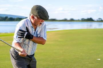 Asian senior man caught injury shoulder while golfing at country club on summer vacation. Elderly male golfer shoulder pain while outdoor sport workout. Senior people medical and healthy care concept - Powered by Adobe