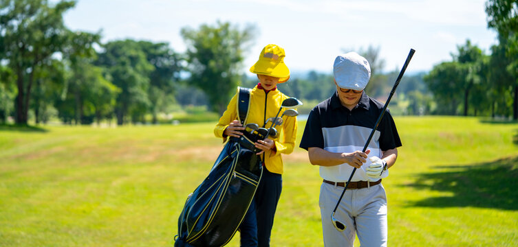 Asian man golfer walking on fairway together with female caddy on the green at golf course in sunny day. Healthy male enjoy outdoor lifestyle activity sport golfing at country club on summer vacation