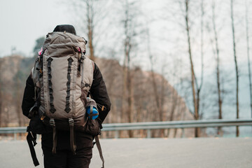 Portrait of an Indian traveler wearing hiking bag standing on the side of the road at Manali in Himachal Pradesh, India. Hitchhiker waiting for the vehicle besides road